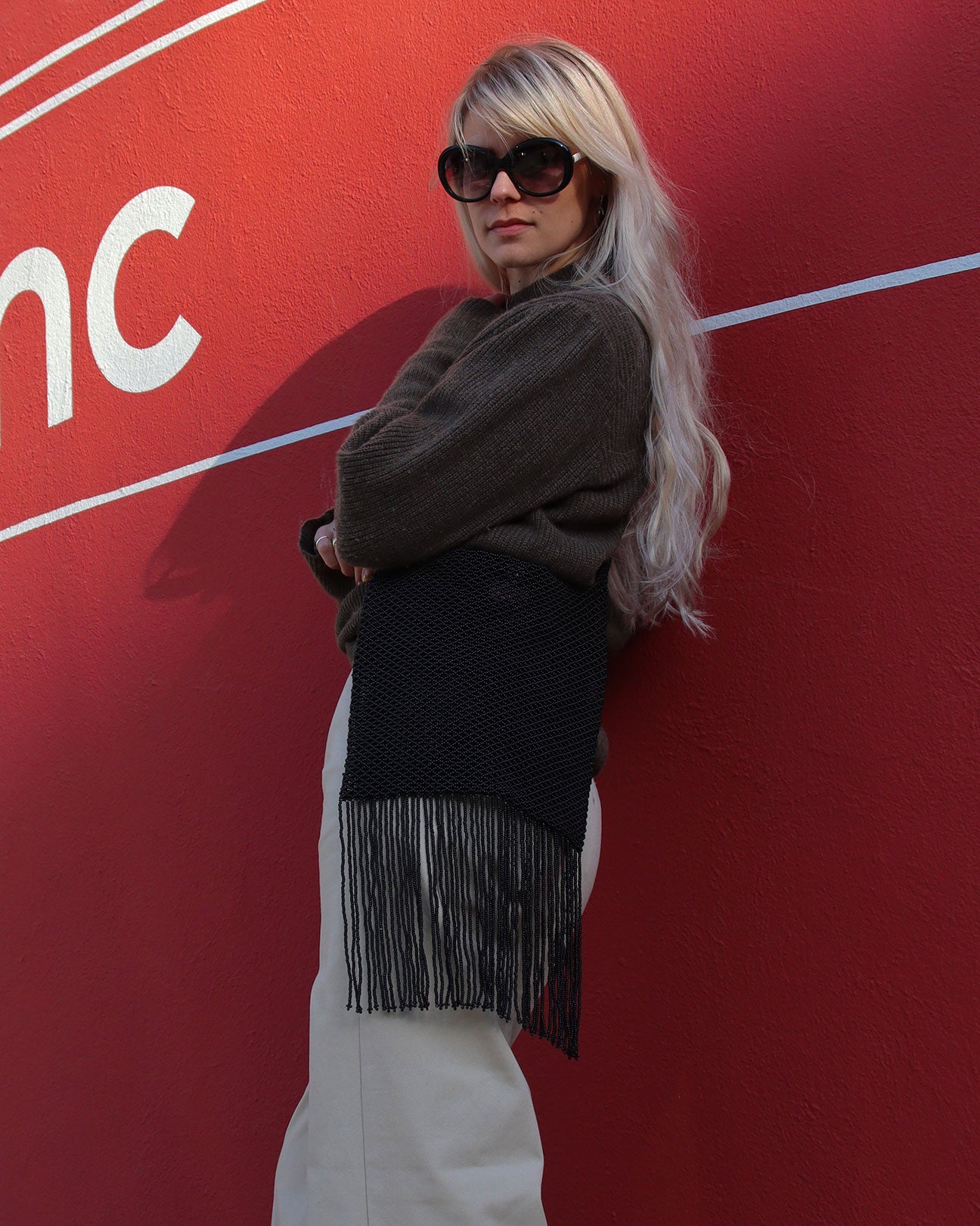 Marmaclub Crossover Fringe Black bag with model in white trousers in front of a red wall
