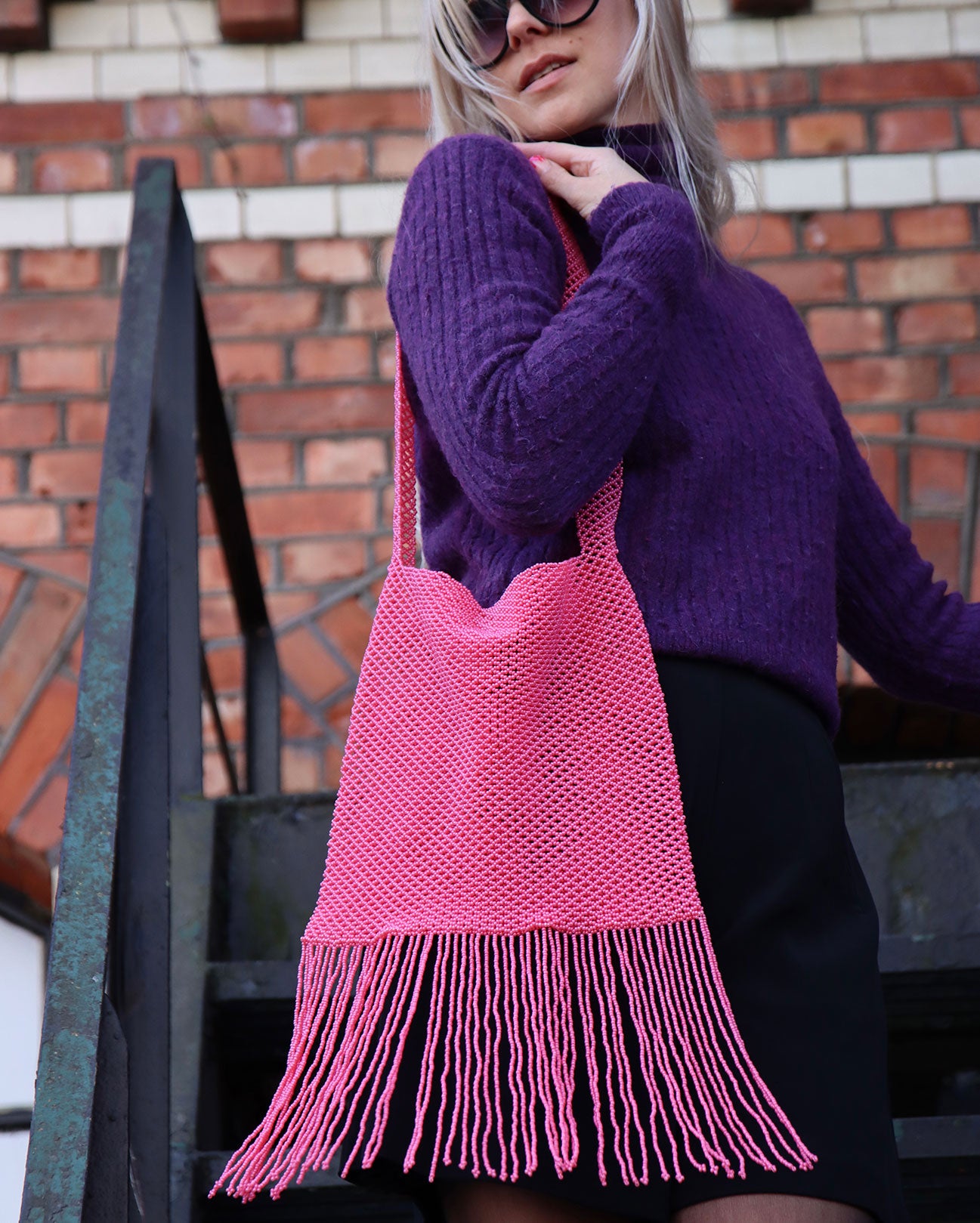 the Marmaclub Crossover Fringe Hot Pink on model in purple sweather and black skirt in a steep stair ers in front of a red wall